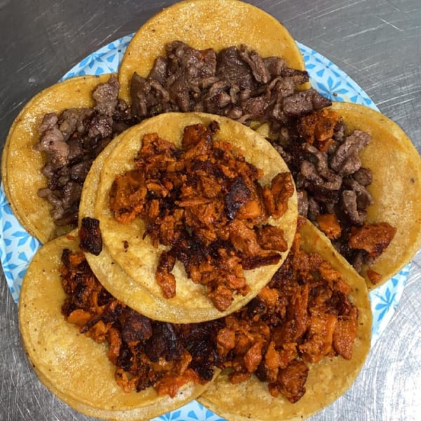 A plate of six tacos, three with dark red meat and three with brown meat, on corn tortillas.